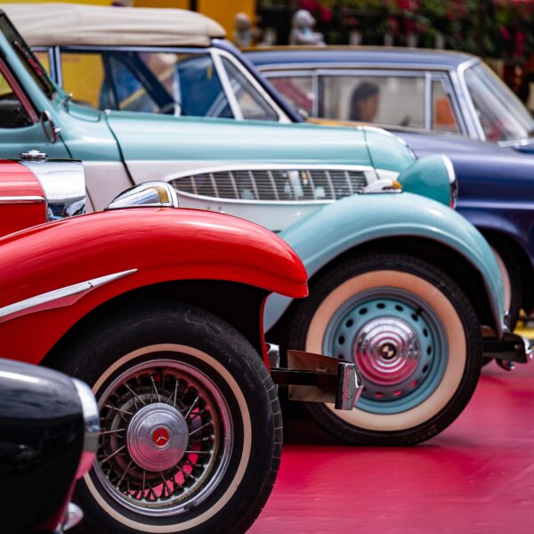 Four classic cars in black, red, teal, and blue are displayed at a car show. Photo by Peter Xie from Pexels