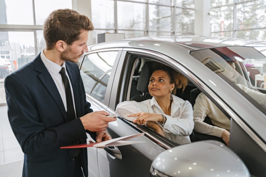 A car salesman hands over a key to a woman in her new car.
Photo by Antoni Shkraba from Pexels