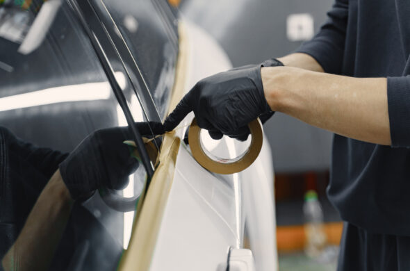 A gloved hand tapes a car in preparation for a paint job. Photo by prostooleh from Magnific