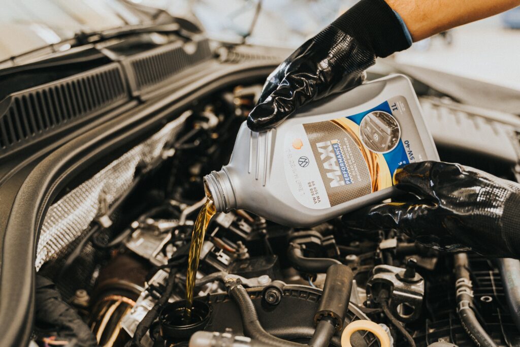 A gloved hand working under the hood of a car pours oil from a jug into a spout.
Photo by Daniel Andraski from Pexels