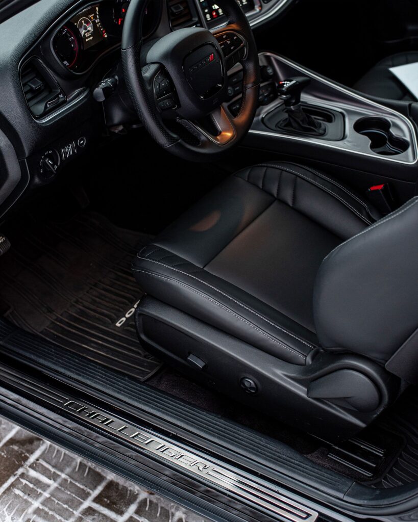 A black car mat nestled on the floor of a black and chrome car interior.
Photo by Ivan Kazlouski from Pexels.