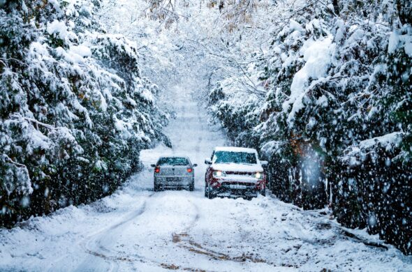 Two cars try to navigate a snowy street lined by snow covered trees. Photo by Hilmi Işılak from Pexel