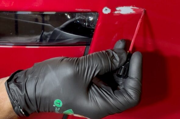 A hand wearing a black TouchUpDirect wearing glove paints a scratch on a red car.