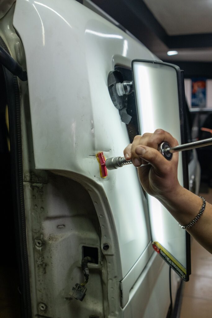 Close-up of vehicle dent repair in a garage using specialized tools under bright lighting.
Photo by Melih Can from Pexels