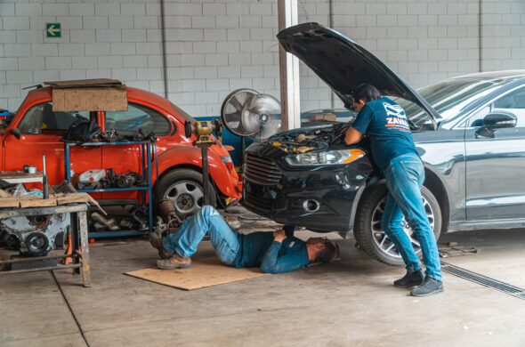 Two repairmen work on a black car. One under the hood. One under the car. Photo by Jose Ricardo Barraza Morachis from Pexels