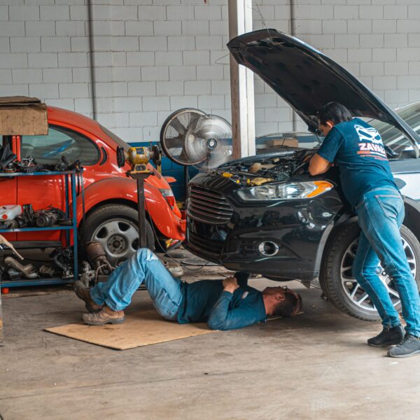Two repairmen work on a black car. One under the hood. One under the car. Photo by Jose Ricardo Barraza Morachis from Pexels