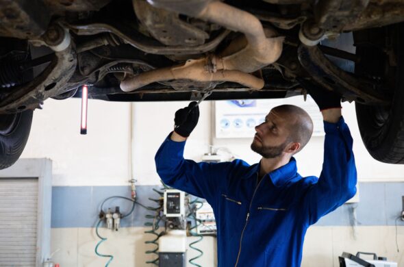 A man stands under a car on a car lift, working on the underside. Photo by Artem Podrez from Pexels