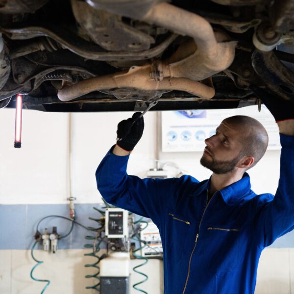 A man stands under a car on a car lift, working on the underside. Photo by Artem Podrez from Pexels