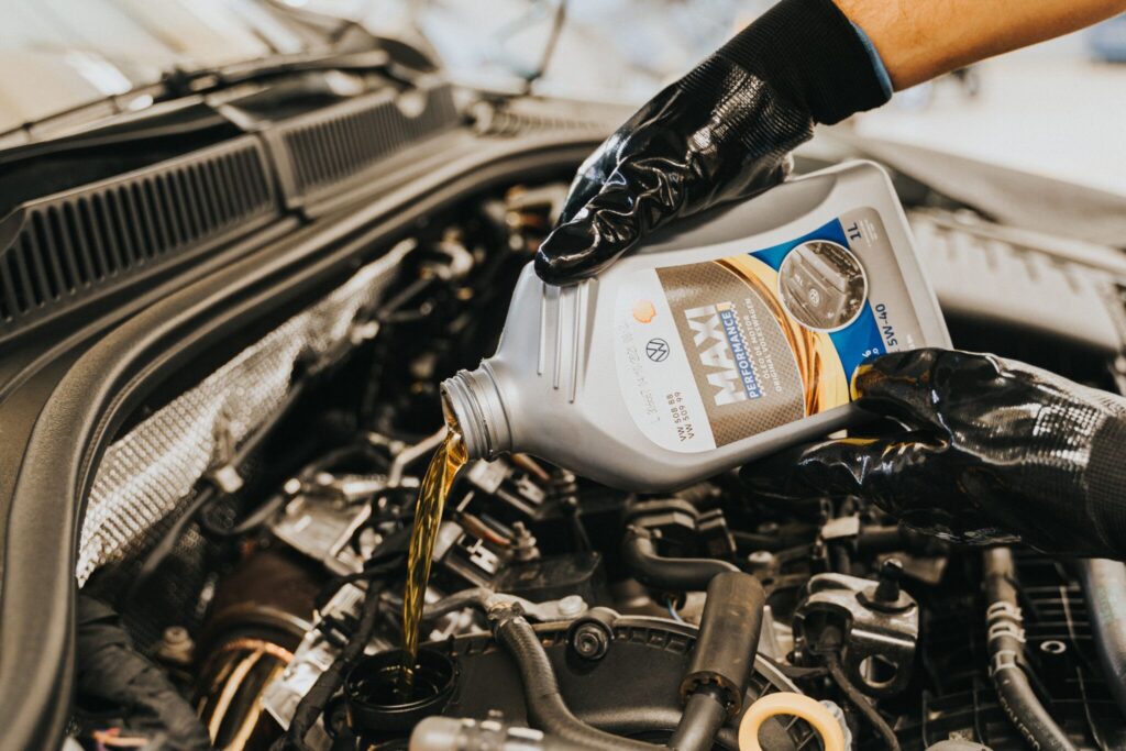 Gloved hands working under the hood of a car pours a jug of oil into a spout in the mechanics.
Photo by Daniel Andraski from Pexels.