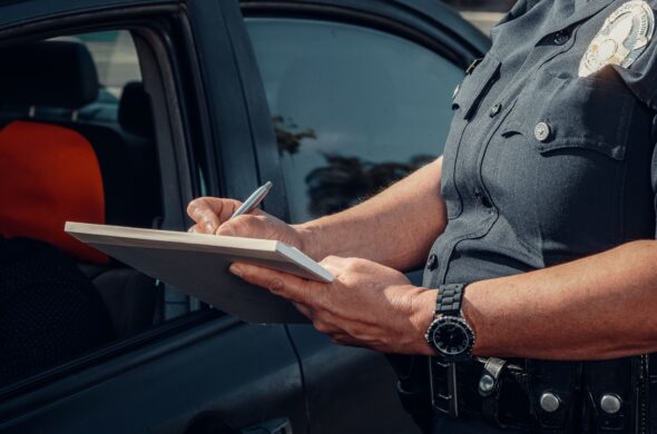 A police officer writes a ticket for an unseen driver. Photo by Kindel Media from Pexels
