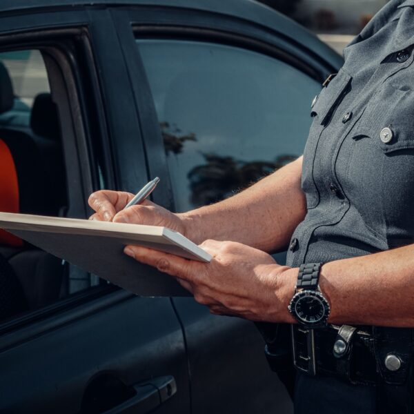A police officer writes a ticket for an unseen driver. Photo by Kindel Media from Pexels
