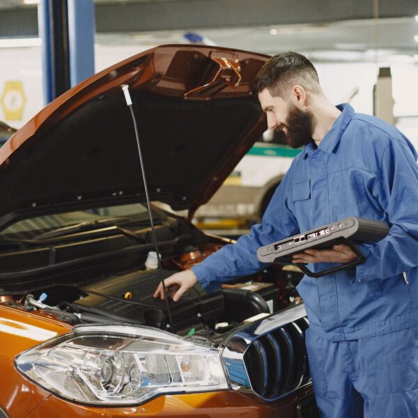 A mechanic inspects under the hood of an orange car. Photo by Gustavo Fring from Pexels