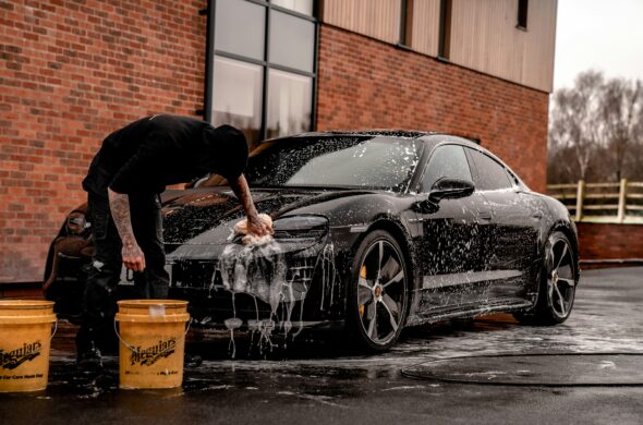 A man cleans his black car in front of a brick building. Photo by Brad Starkey from Unsplash