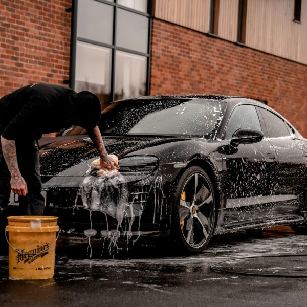 A man cleans his black car in front of a brick building. Photo by Brad Starkey from Unsplash