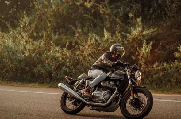 A person drives a black motorcycle on a road lined by trees Photo by Abhishek sanga from
