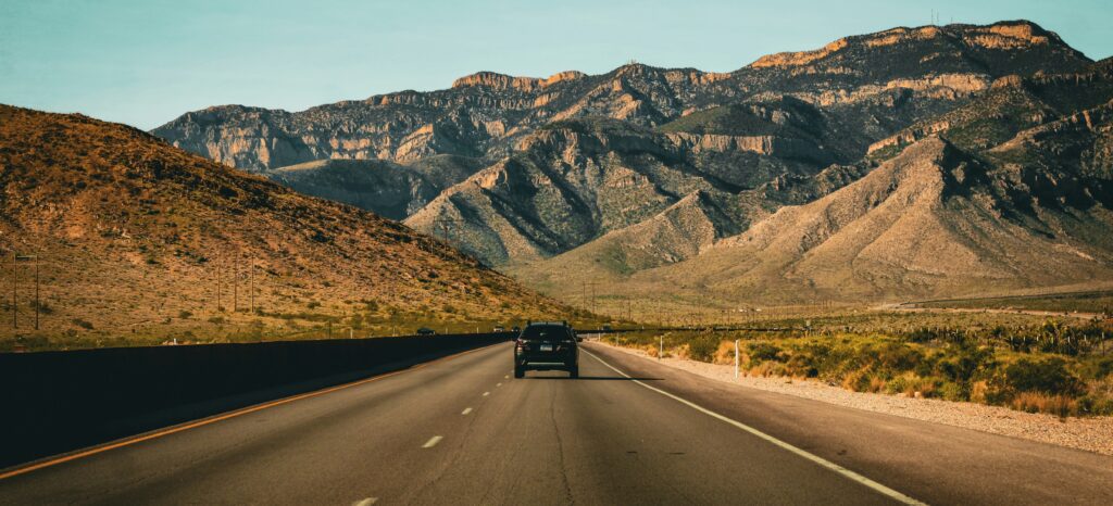 A car drives down a road with mountains in the distance.
Photo by Victor Svistunov