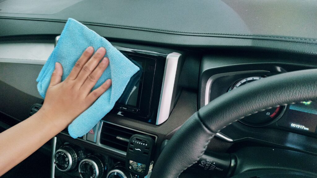 A hand wipes down a console in the car's interior with a blue towel. Photo by Ariyo from Pexels