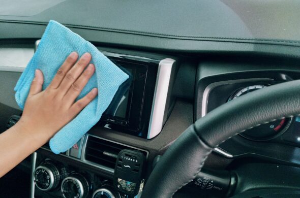 A hand wipes down a console in the car's interior with a blue towel. Photo by Ariyo from Pexels