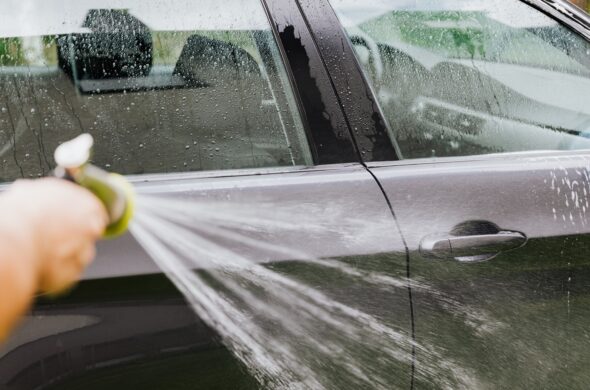 A hand sprays a black car with a hose. Photo by Kaboom Pics from Pexels