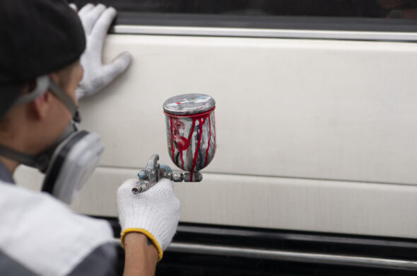 A properly masked man spray paints a white car. Photo from Magnify.