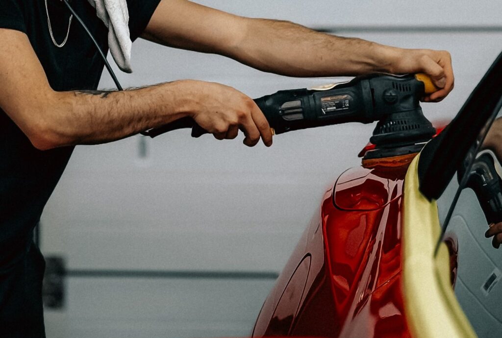 A pair of arms polishes a metallic red car. Photo by Bulat843 from Pexels
