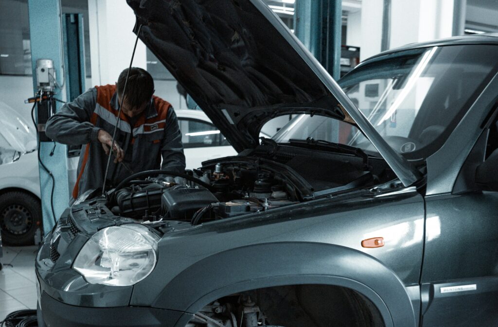A mechanic works under the hood of a gray SUV. Photo by Kate Ibragimova from Pexels