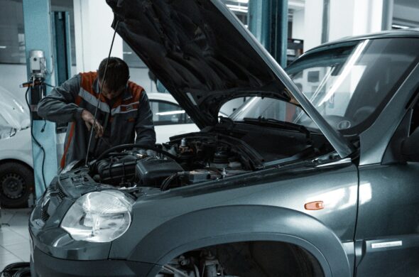 A mechanic works under the hood of a gray SUV. Photo by Kate Ibragimova from Pexels
