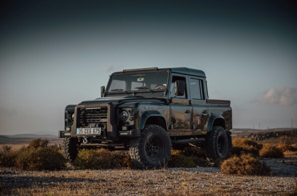A Restored Land Rover Defender in British Race Green sits in a field. Photo by Phillipe Berk de Andria from Unsplash