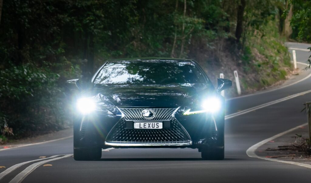 A black Lexus with hits headlights on drives down a winding path by the woods. Photo by Max Ravier from Pexels