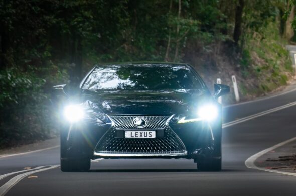 A black Lexus with hits headlights on drives down a winding path by the woods. Photo by Max Ravier from Pexels