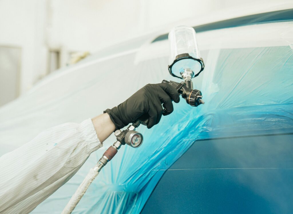 A hand wearing a black glove spray paints a car blue. Photo by Dylan Calluy from Unsplash