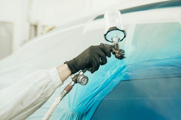 A hand wearing a black glove spray paints a car blue. Photo by Dylan Calluy from Unsplash