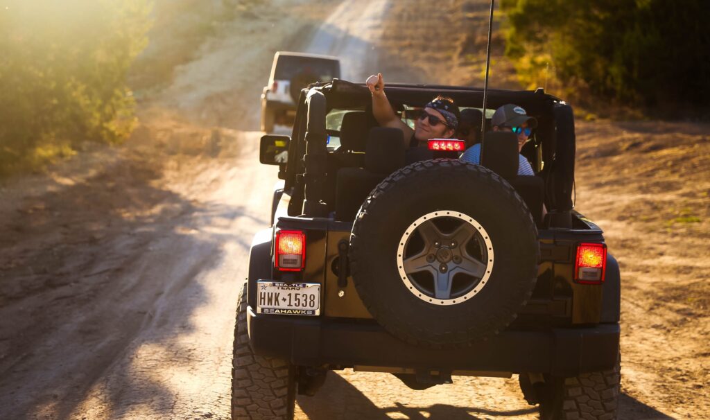 A group of friends in a Jeep greet people the car behind them. Photo by Oliver Schlotfeldt from Pexels
