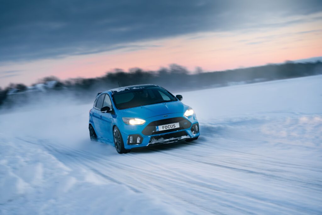 A blue Ford Focus drifting on a snowy rural road at sunset. Photo by Alari Tammsalu
