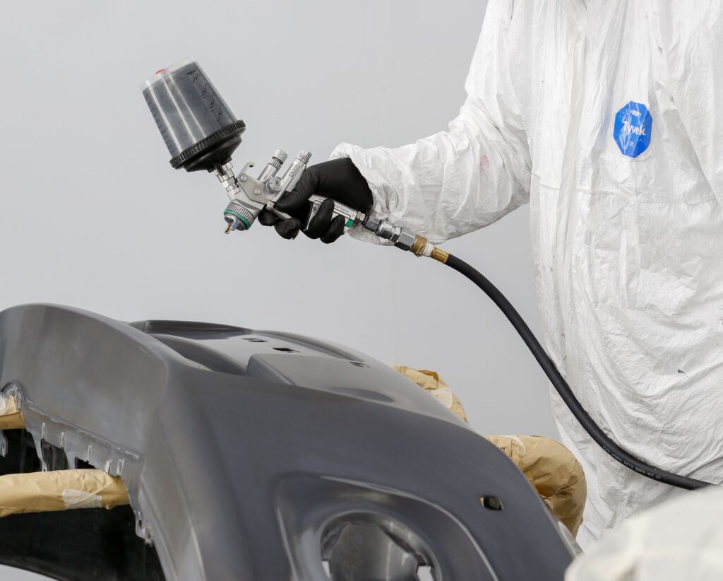 A hand spray paints a gray car panel. Photo by Mohammad Hammad from Pexels