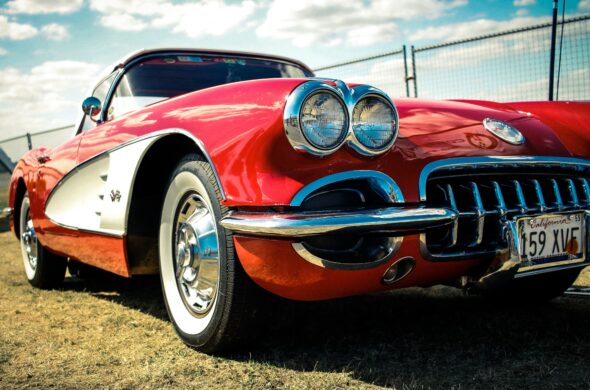 A red and white vintage Chevrolet Corvette parked in the grass at a car show. Photo by Nalin Patinayake from Unsplash