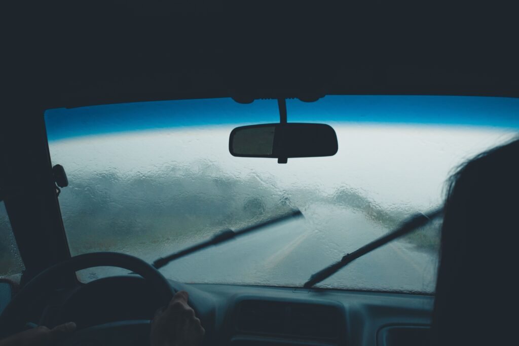 The view from the front seat as rain pelts the windshield. The wipers are in mid wipe. Photo by Lucas Pezeta from Pexels