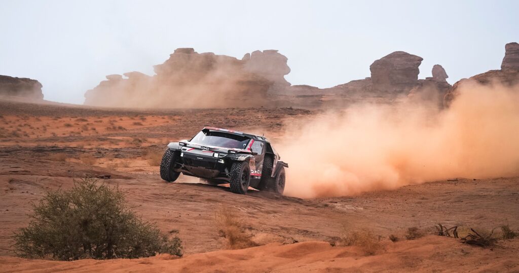 A dynamic off-road rally car kicking up dust on a desert landscape with rock formations. Photo by Fatih Dağlı