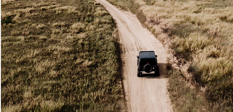 Aerial-view-of-car-driving-by-straight-ground-road-through-fields